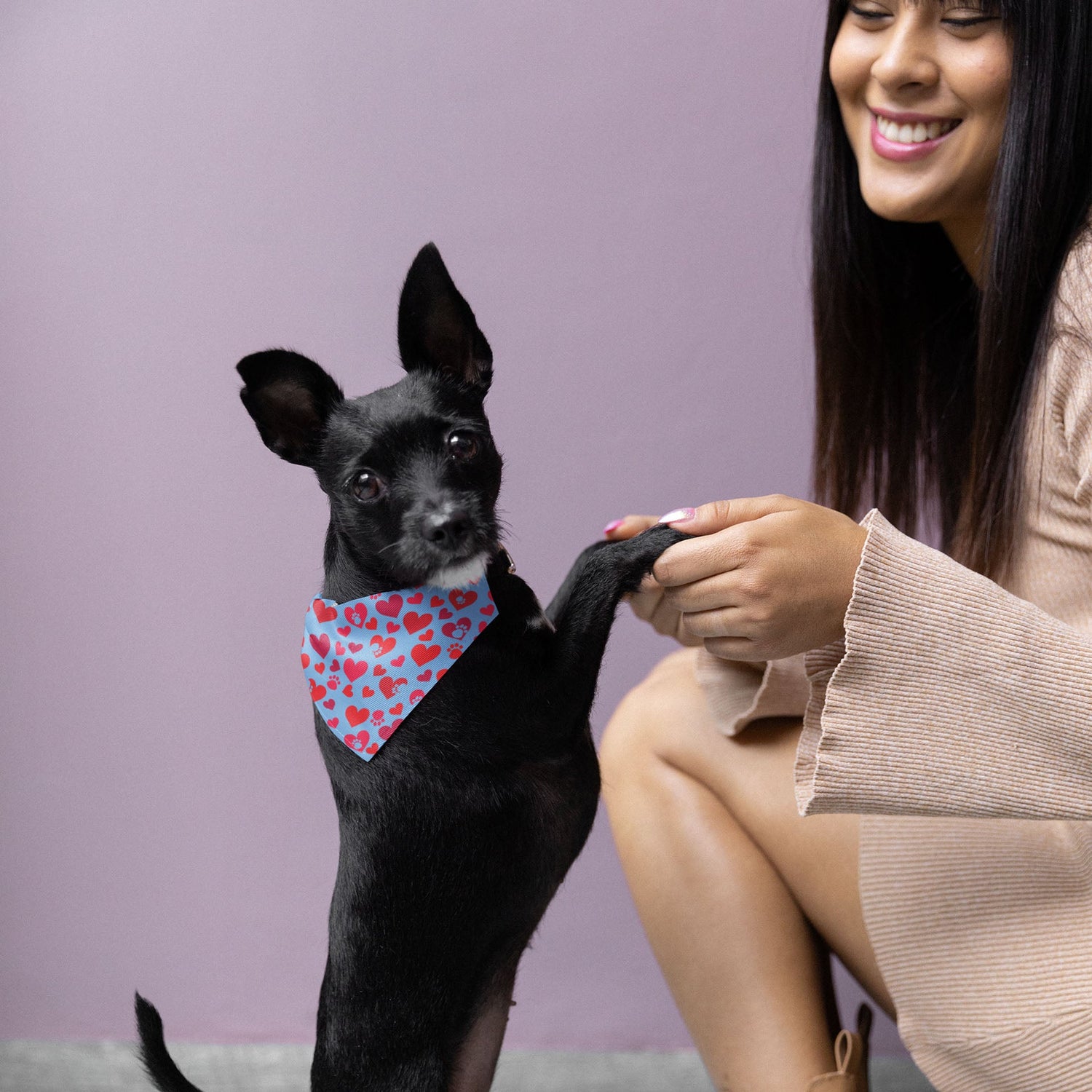  A young woman sits with a radiant smile, gently supporting her Chihuahua's front legs as it stands proudly upright beside her, wearing a Dogs Pure Love bandana