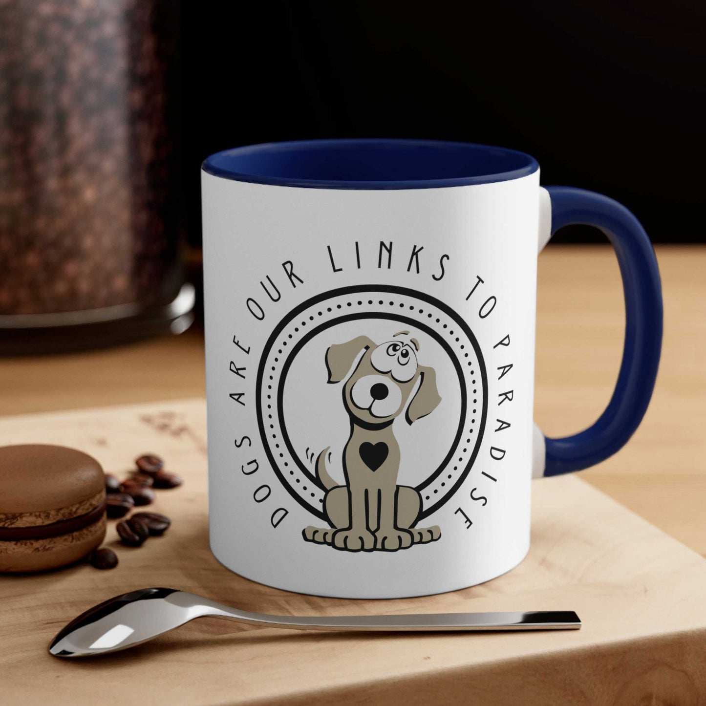 On a table adorned with a biscuit, spoon, and scattered coffee beans, sits a navy and white 'Dogs are Paradise' ceramic mug by Dogs Pure Love. 