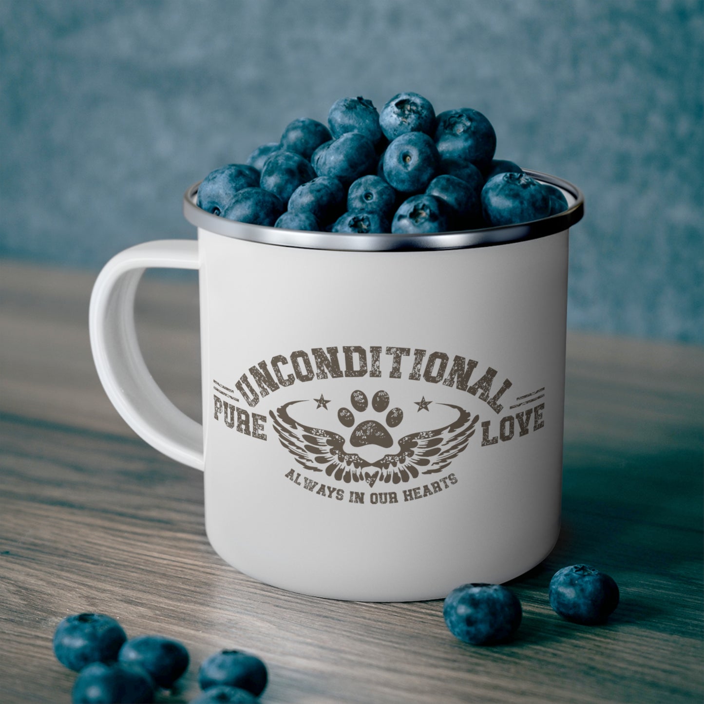  On a table, there's a Dogs Pure Love 12 oz enamel mug with the print 'Unconditional Pure Love, always and forever,' slogan, filled with blueberries.