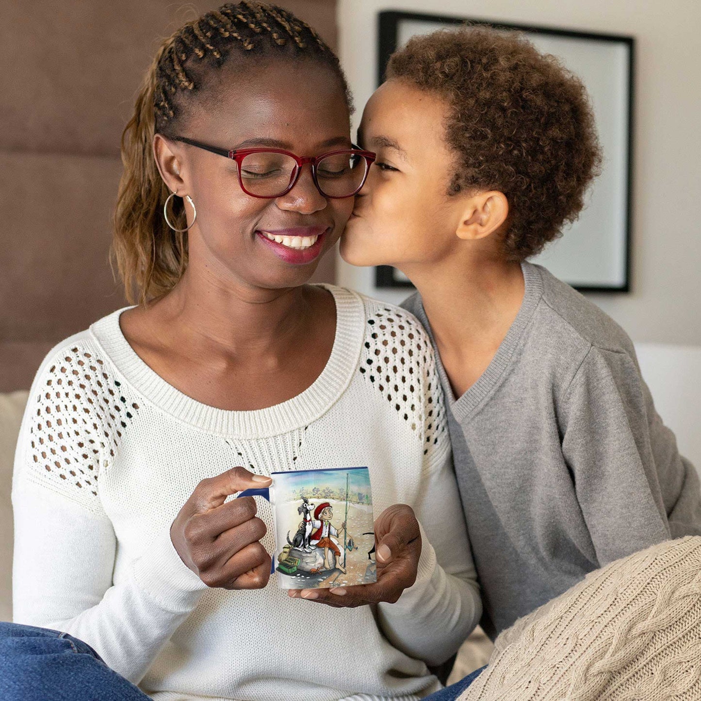 A young boy kisses his mother who sits holding a Dogs Pure Love ceramic mug.