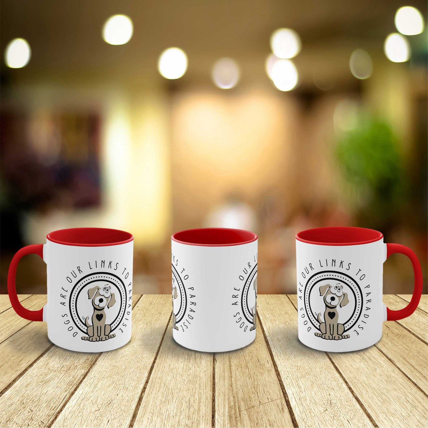 Three two-toned red and white 'Dogs Pure Love, Dogs are Paradise' ceramic mugs are lined up on a wooden bench, to showcase the designs from all angles, the background is a colorful blur.