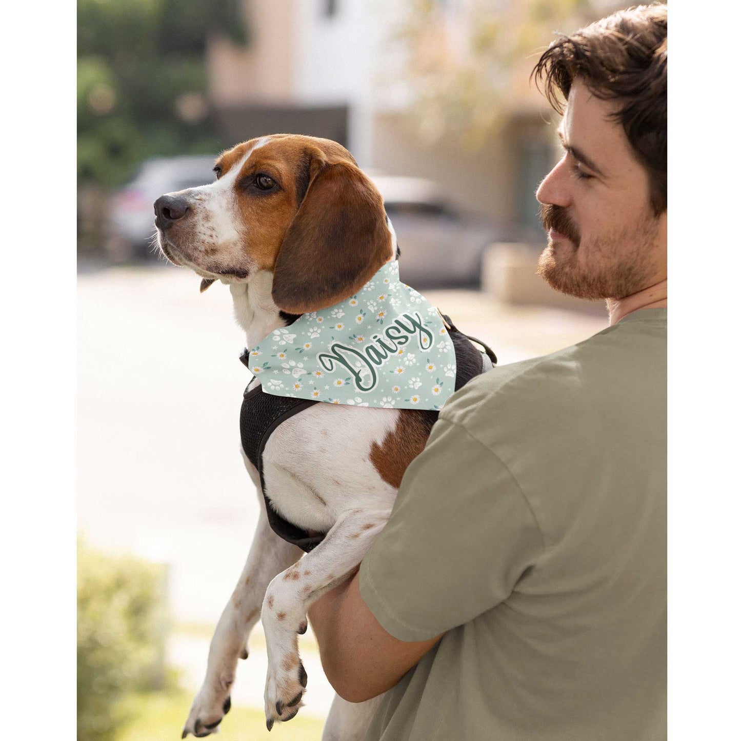 A man holds his dog who is wearing a Dogs Pure Love bandana with the name 'Daisy' on it.