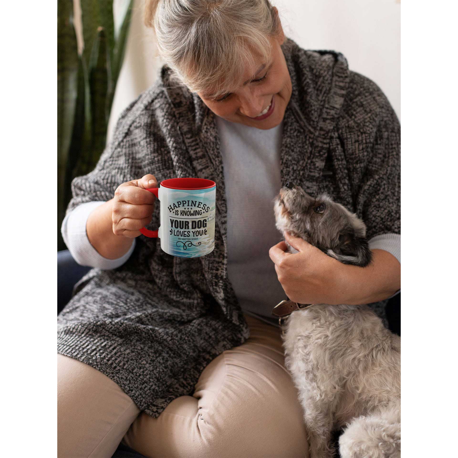  A woman sits, cradling her 'Dogs Pure Love' ceramic 'Happiness Is' mug, while cuddling her small terrier dog.