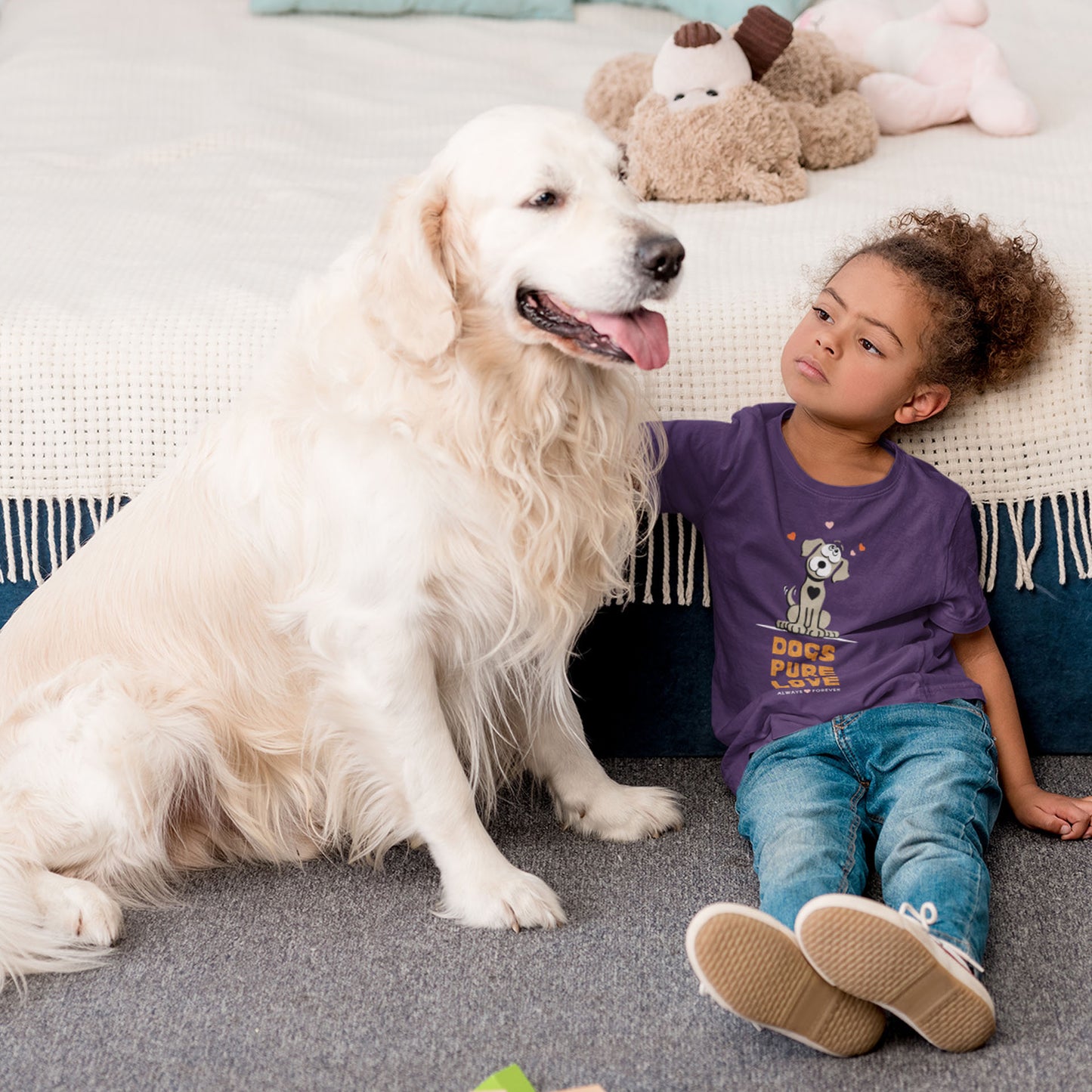  A young girl, dressed in a Dogs Pure Love purple tee, sits on the floor, looking at and patting her Golden Retriever.
