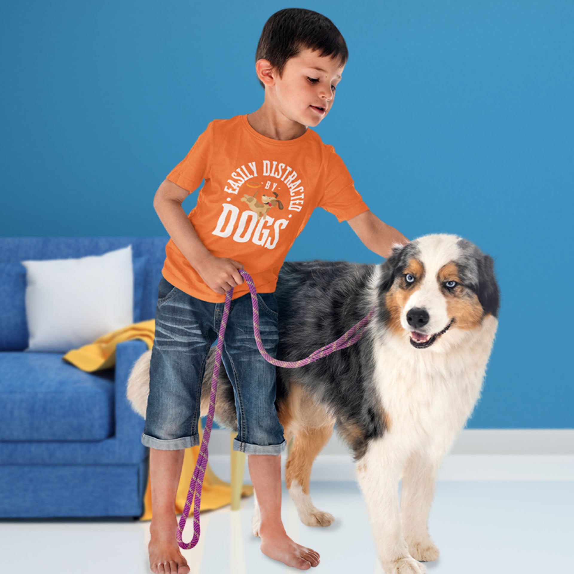  In a living room, a young boy wearing a Dogs Pure Love tee with the print 'Easily Distracted by Dogs' holds a leash and pats a Husky beside him.