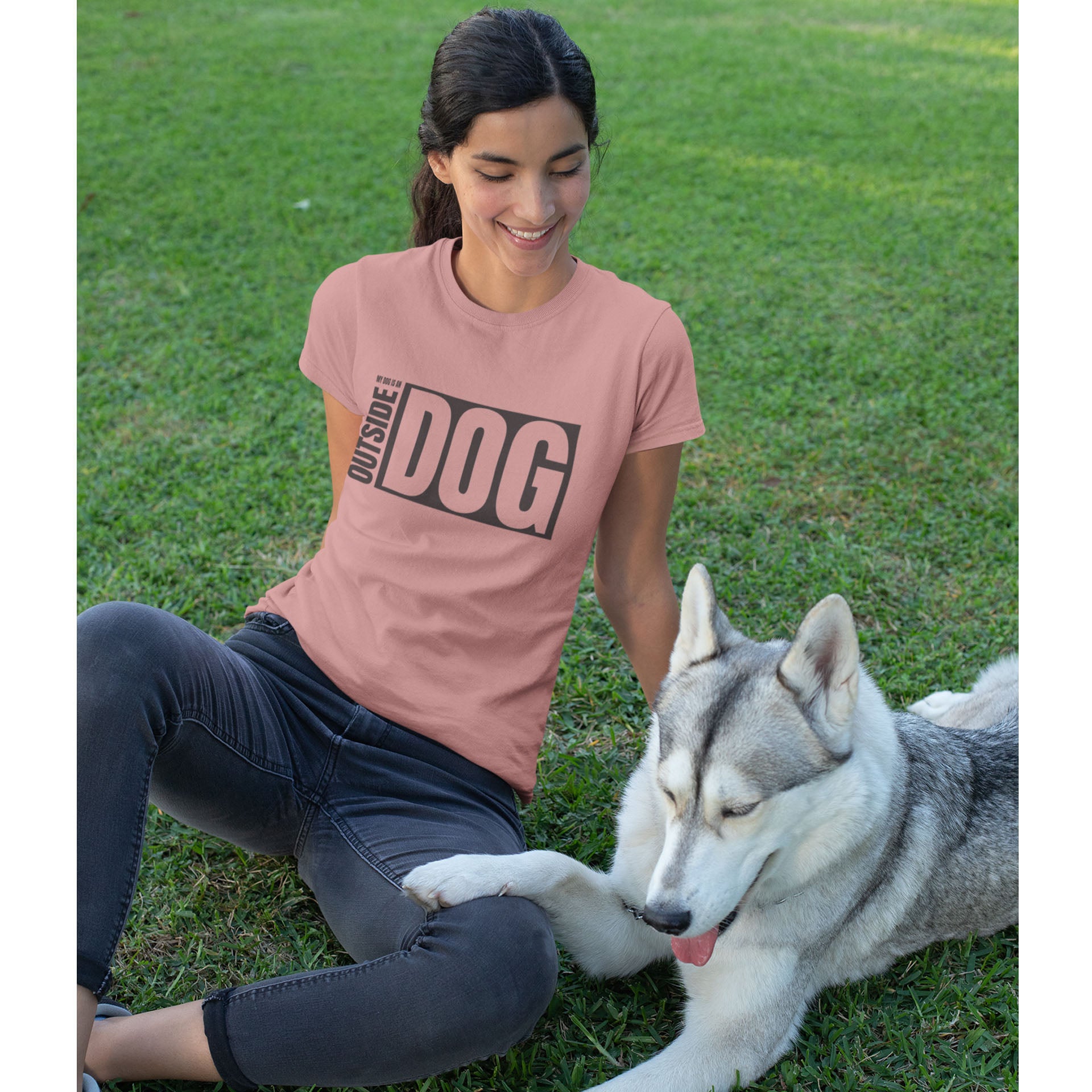  A woman, dressed in the 'Outside Dog' mauve Dogs Pure Love tee, sits on the grass with her Husky, who affectionately rests its paw on her leg.