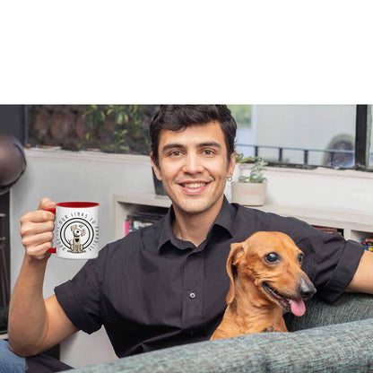 A man holds his Dogs Pure Love 11 oz ceramic two-tone mug, adorned with the 'Dogs are Paradise' slogan and graphic, as he sits on a sofa with his Dachshund.