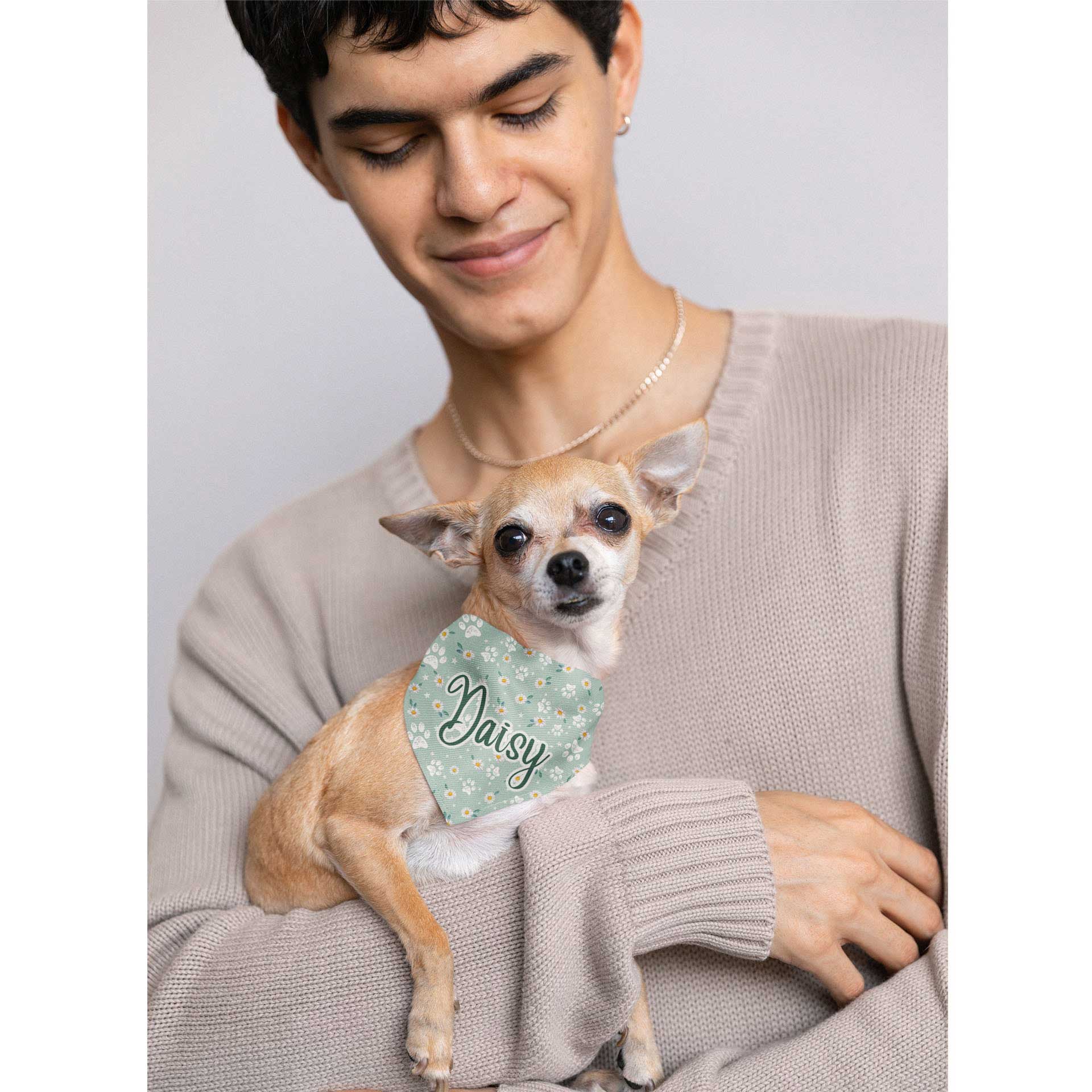  A man holds a Chihuahua wearing a bandana with the name 'Daisy' written on it.