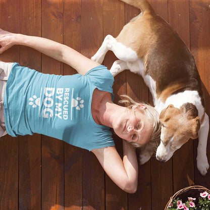 A woman wears a Dogs Pure Love, 'Rescued by my Dog' t-shirt, with her dog laying near her on a wooden floor.