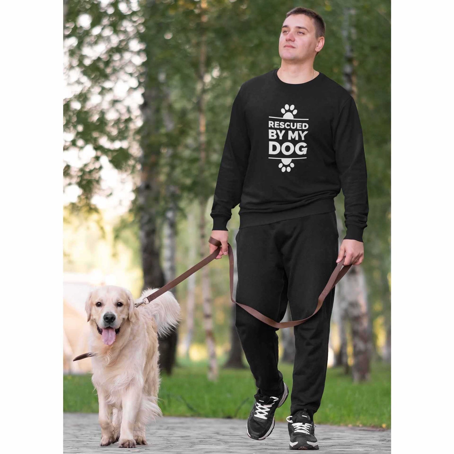  A man strolls on a footpath with his Golden Retriever near the woods, he wears a Dogs Pure Love sweatshirt with the text 'Rescued by my Dog.'