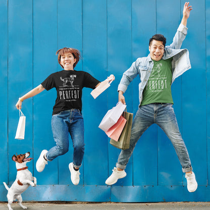  A Jack Russell terrier leaps onto its hind legs while a couple joyfully jumps into the air, both adorned in Dogs Pure Love, Unperfected tees, set against a backdrop of a vibrant blue wall.