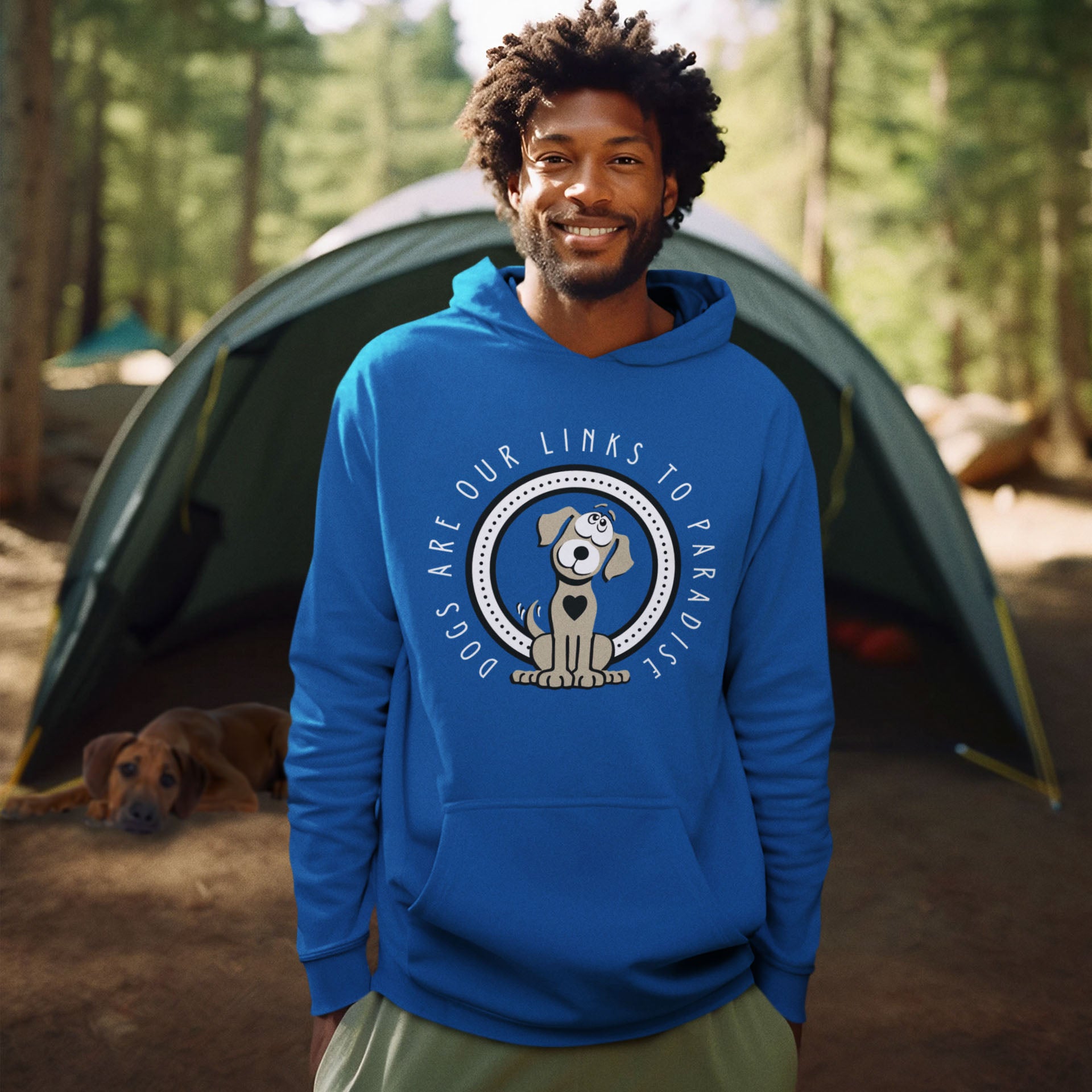  A man, donning a royal blue 'Dogs are Paradise' hoodie by Dogs Pure Love, stands with a smile, hands casually tucked in his pockets. In the background, his dog rests partially inside a tent in a forest setting.