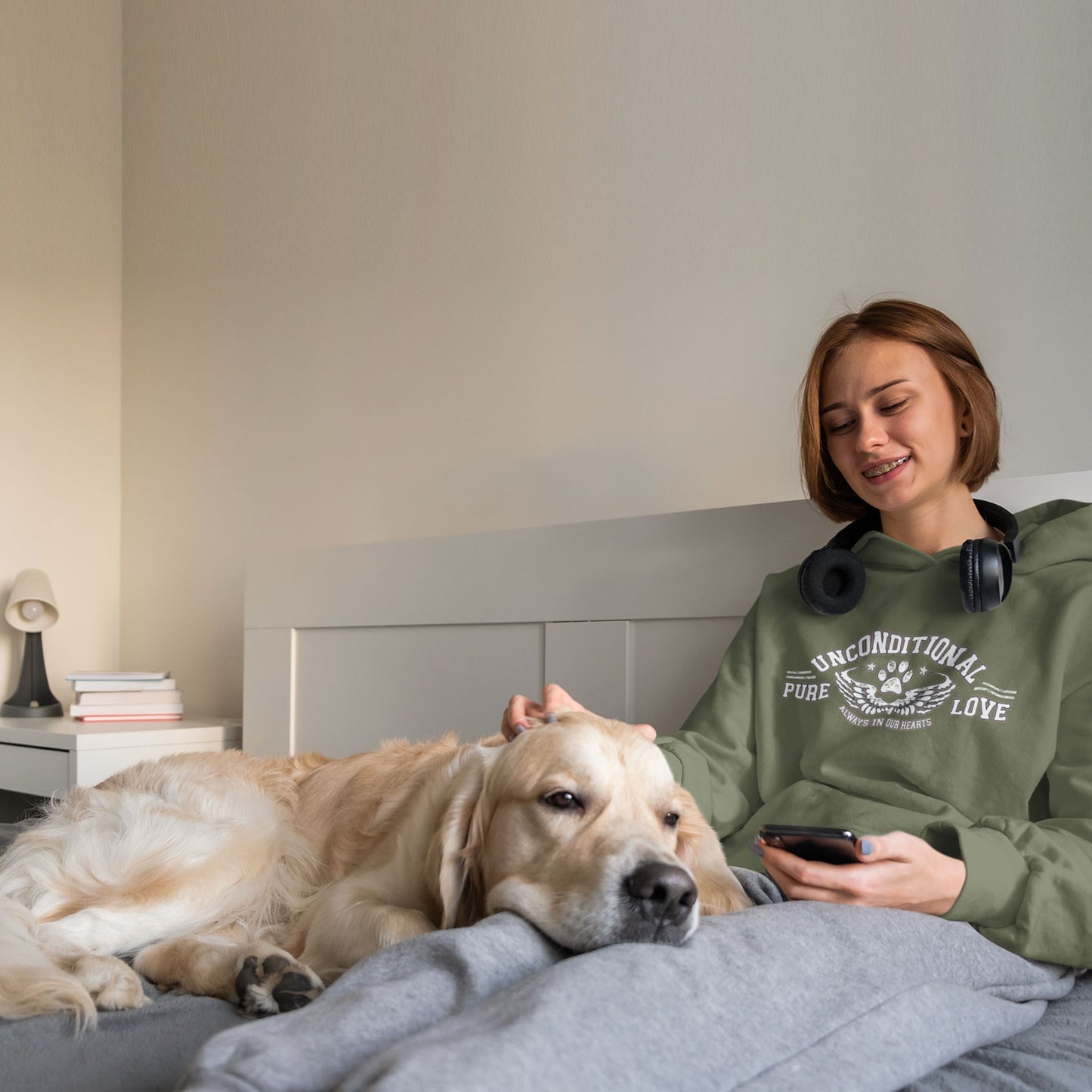 Golden Retriever lays on the lap of a young girl in bed wearing a' Dogs Pure Love, Urban Paws' green unisex hoodie. 