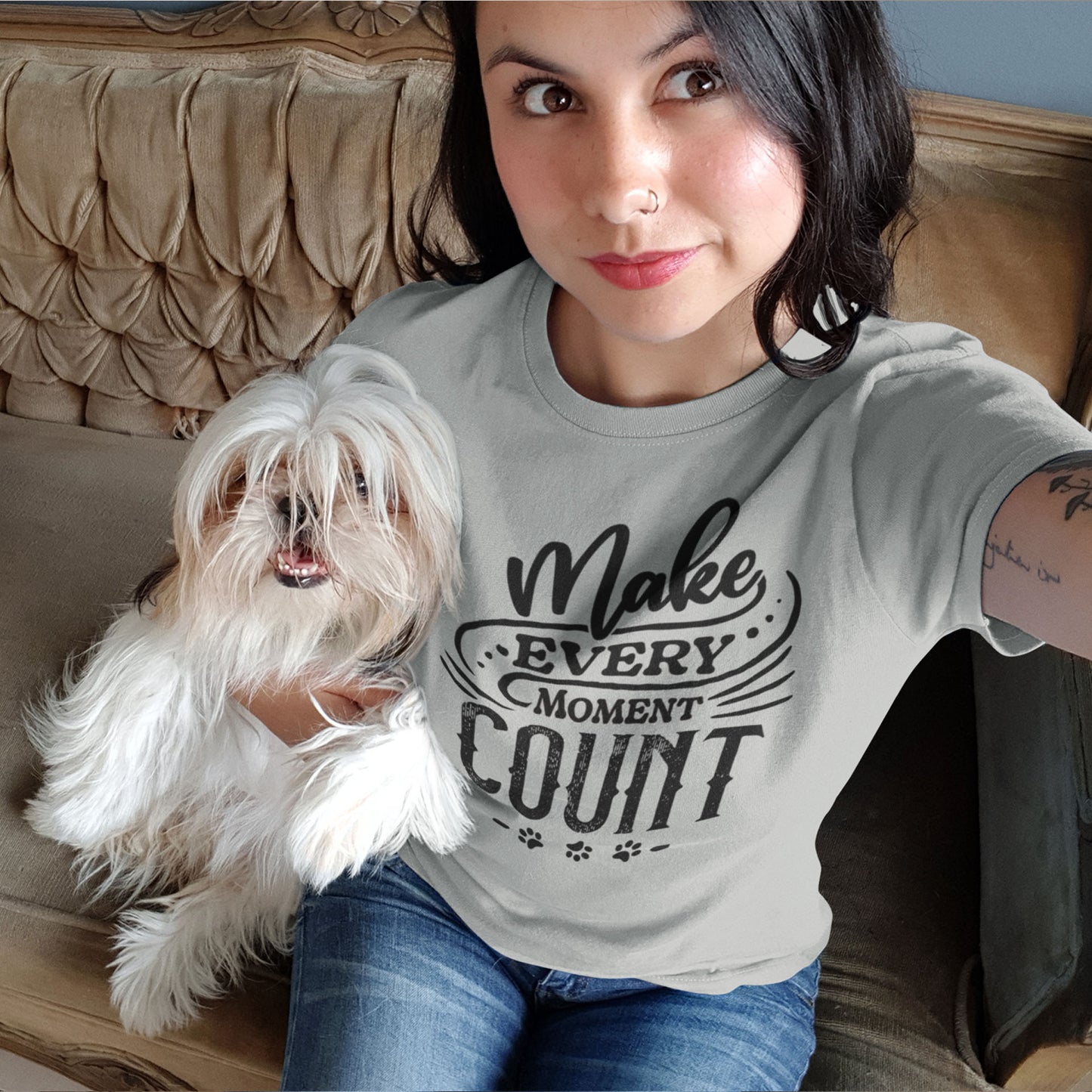  A woman wearing a Dogs Pure Love tee with the slogan "Make Every Moment Count" sits on the sofa, taking a selfie with her Affenpinscher dog.