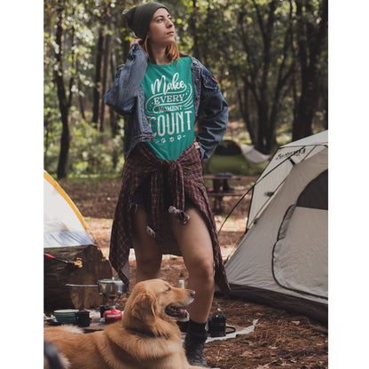  A woman stands in her campsite wearing a Dogs Pure Love tee with the inspiring slogan "Make Every Moment Count." She sports a beanie and has a shirt wrapped around her waist, while her Golden Retriever accompanies her near a cooker.