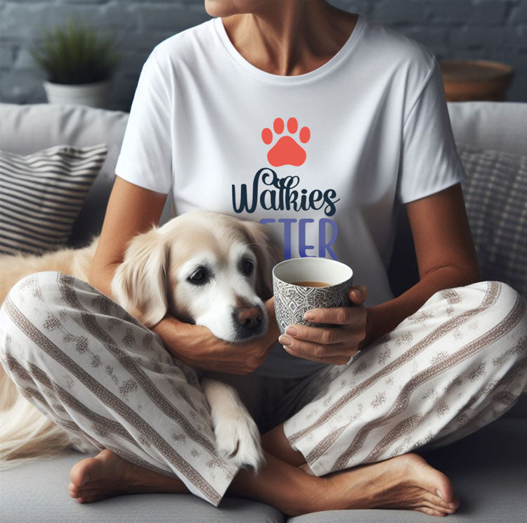  A woman wearing pajama bottoms and a 'Dog's Pure Love, Walkies After Coffee' tee sits on the floor with a Golden Retriever and a cup of coffee.