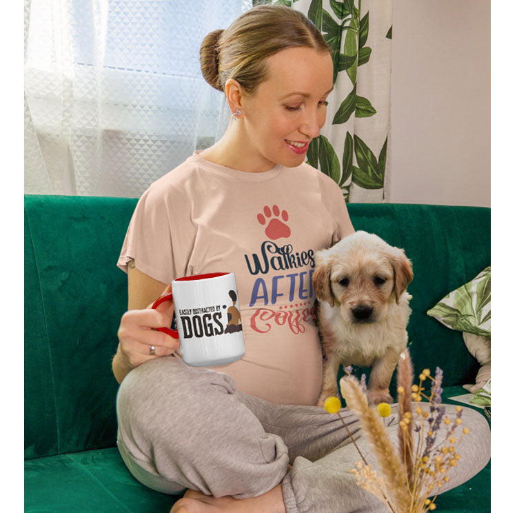  A pregnant woman, clad in a 'Dog's Pure Love, Walkies After Coffee' tee, relaxes on her couch with a cup of coffee in one hand and a Golden Retriever puppy in the other.