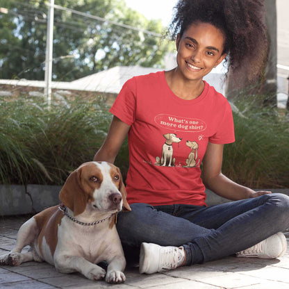 A young woman sits next to her dog smiling, she is wearing a Dogs Pure Love red tee with  a print that has two dogs looking at each other and a speech bubble that reads 'Whats one more dog shirt.'