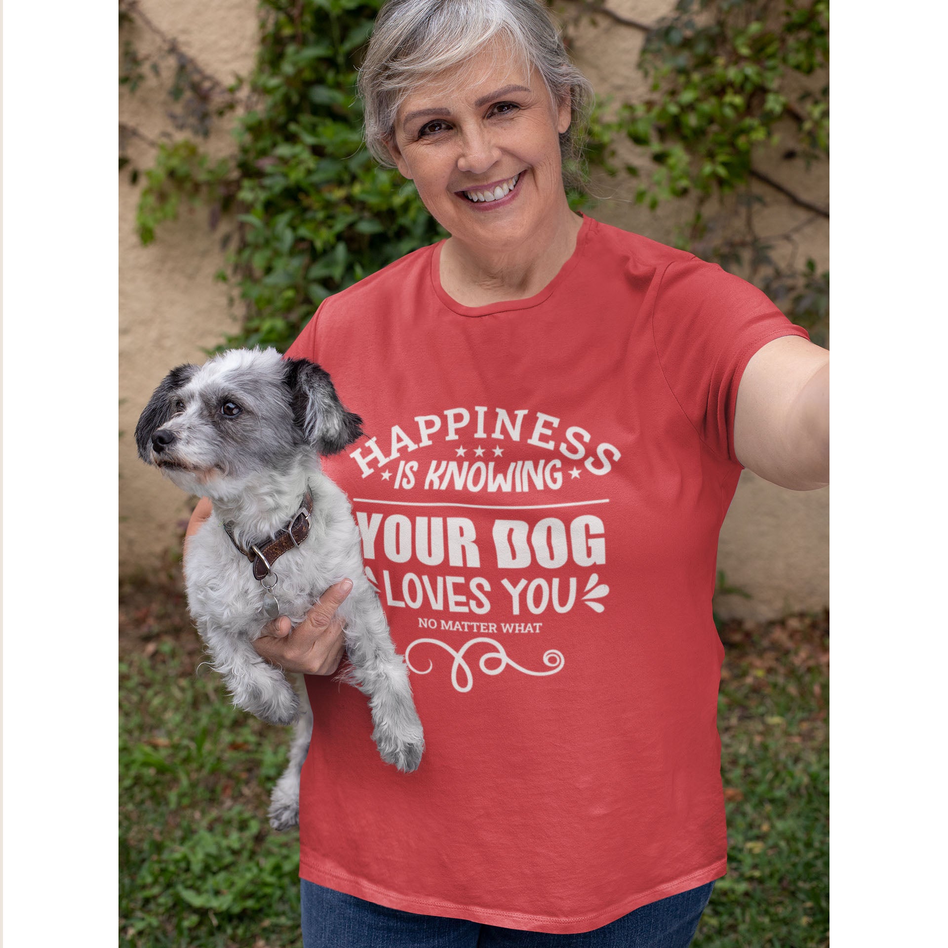 A woman wearing a 'Dogs Pure Love' tee holds her dog, against a background of vines and grass.