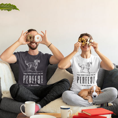  A young couple lounges on the couch, both sporting Dogs Pure Love 'Unperfected' tees, playfully holding two donuts each over their eyes. A puppy dog rests peacefully curled up on the woman's lap.